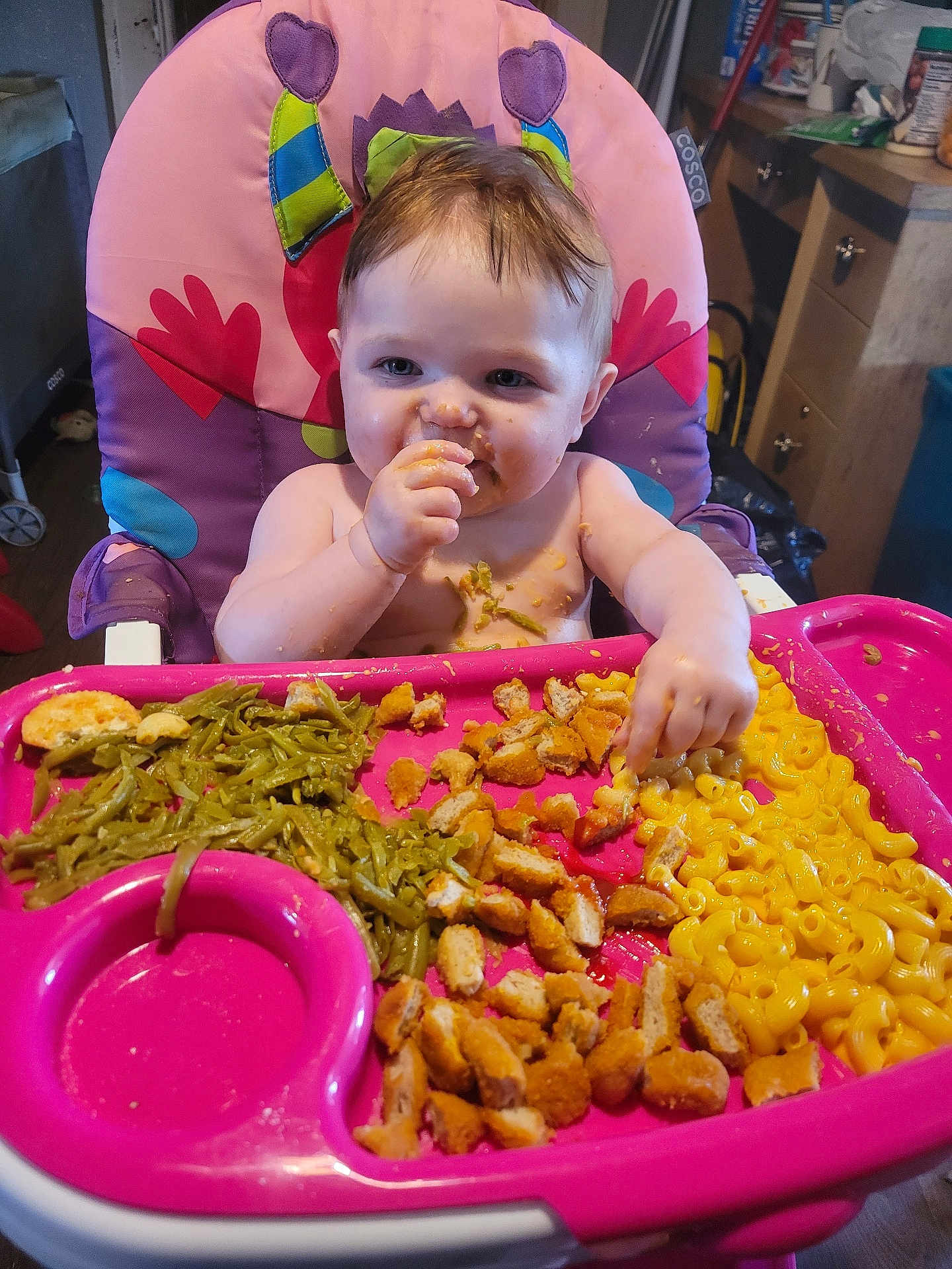 Luna joined the competition — help win amazing prizes! baby, high_chair, food, green_beans, chicken_nuggets, macaroni_and_cheese, messy, eating, child, indoor, pink_tray, face, hand, smile, hair, plate, kitchen, person, seat, happy