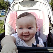 Nevaeh is registered to the contest to win money with this photo: baby, child, clothing, eyes, face, greenery, hand, happy, harness, infant, outdoor, photography, pink, portrait, reaching, sitting, smiling, stroller, suburban, sunlight