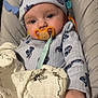 baby, infant, pacifier, beanie_hat, blanket, onesie, baby_seat, hand, face, eyes, cheeks, close_up, portrait, indoor, soft_lighting, muslin_blanket, blue_clothing, patterned_clothing, bouncer, calm_expression
