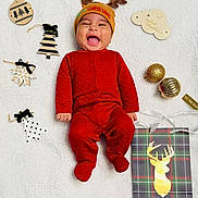 Jake is registered to the contest to win money with this photo: baby, infant, red_onesie, reindeer_hat, christmas_decorations, wooden_ornaments, gold_baubles, white_blanket, smiling, holiday, festive, cute, happy, lying_down, indoors, portrait, seasonal, celebration, child, cozy