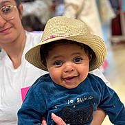 Djalyl a rejoint le concours — aidez-le/la à gagner de superbes lots ! baby, child, hat, straw_hat, blue_sweater, smiling, woman, glasses, person, holding, indoor, portrait, cute, happy, face, clothing, hand, people, infant, casual
