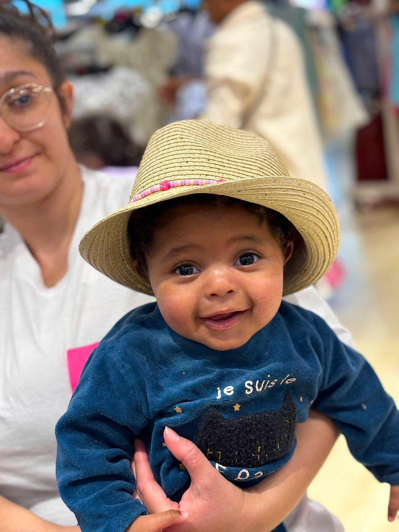 Djalyl a rejoint le concours — aidez-le/la à gagner de superbes lots ! baby, child, hat, straw_hat, blue_sweater, smiling, woman, glasses, person, holding, indoor, portrait, cute, happy, face, clothing, hand, people, infant, casual