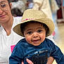 baby, child, hat, straw_hat, blue_sweater, smiling, woman, glasses, person, holding, indoor, portrait, cute, happy, face, clothing, hand, people, infant, casual
