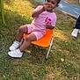 child, outdoor, grass, chair, playground, smiling, pink_clothing, sneakers, happy, fence, shorts, toddler, person, daylight, nature, seat, play_area, casual, young_child, snack