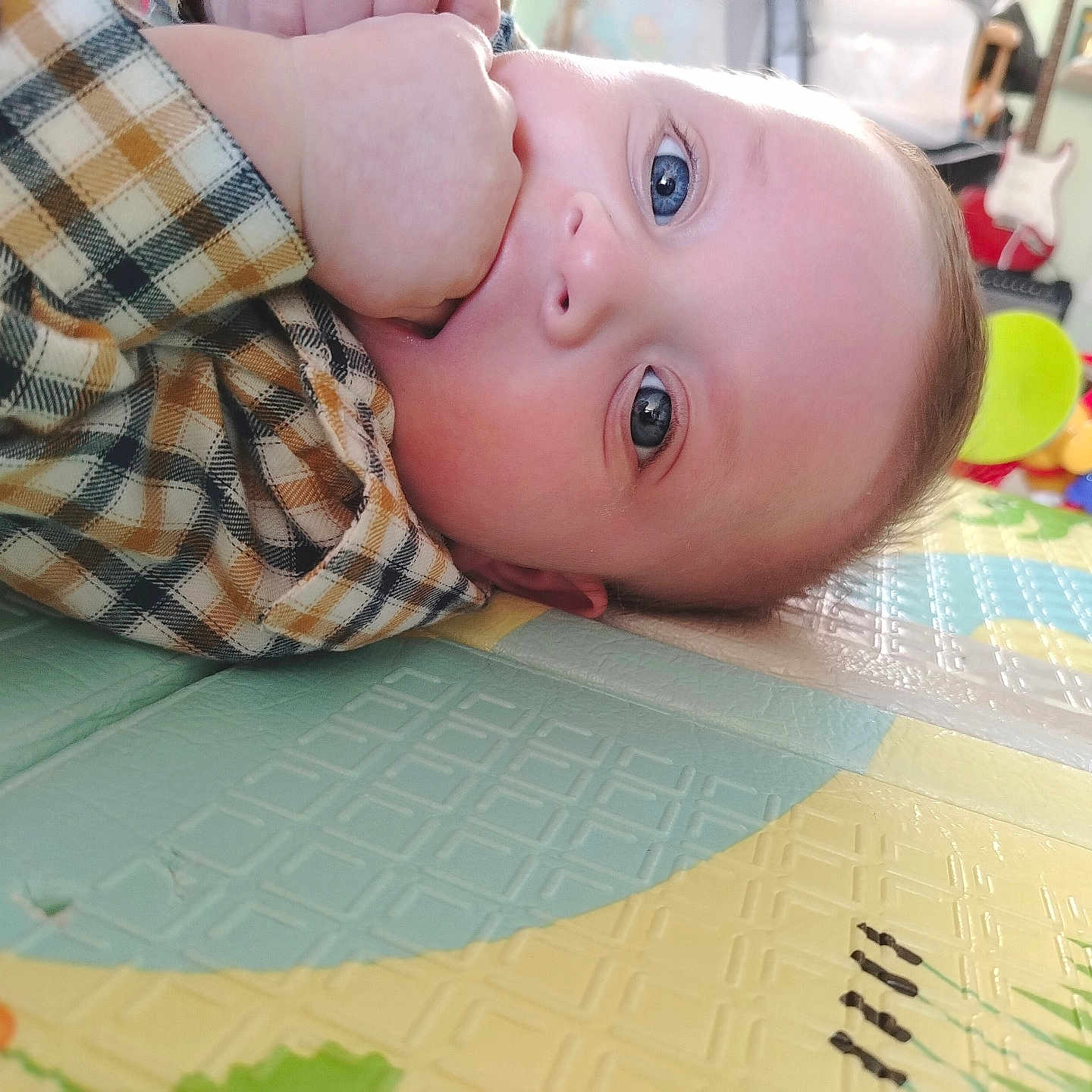 Gaël a rejoint le concours — aidez-le/la à gagner de superbes lots ! baby, blue_eyes, child, closeup, colorful, curious, cute, face, floor, guitar, hand, home, indoor, infant, person, plaid_shirt, play_mat, sitting, toy, young