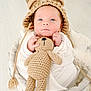 Gaël a rejoint le concours — aidez-le/la à gagner de superbes lots ! baby, infant, knitted_hat, crocheted_toy, teddy_bear, basket, swaddling_cloth, neutral_colors, dried_plants, soft_lighting, portrait, cute, cozy, newborn, face, hands, indoors, sleepy, soft_texture, peaceful