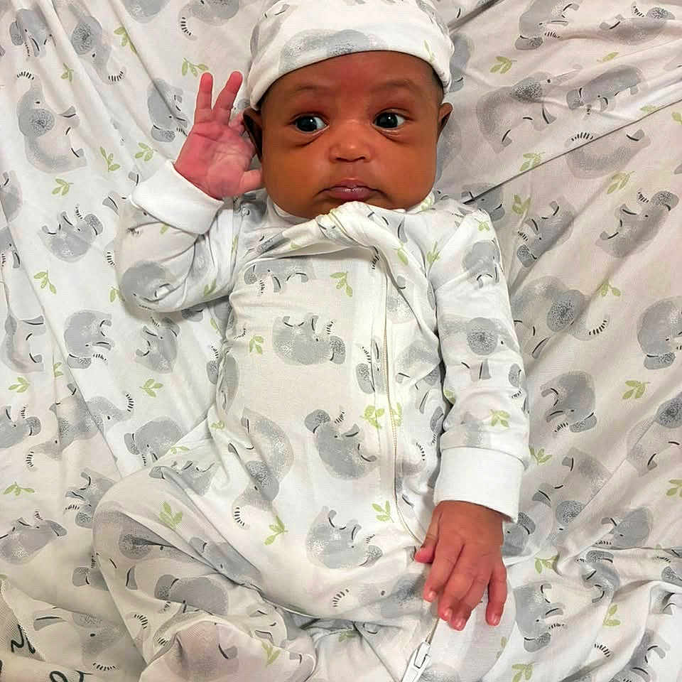 Ryden joined the competition — help win amazing prizes! baby, newborn, infant, child, portrait, lying_down, onesie, hat, blanket, elephant_pattern, nursery, indoors, face, eyes, hand, wave, awake, closeup, textile, adorable