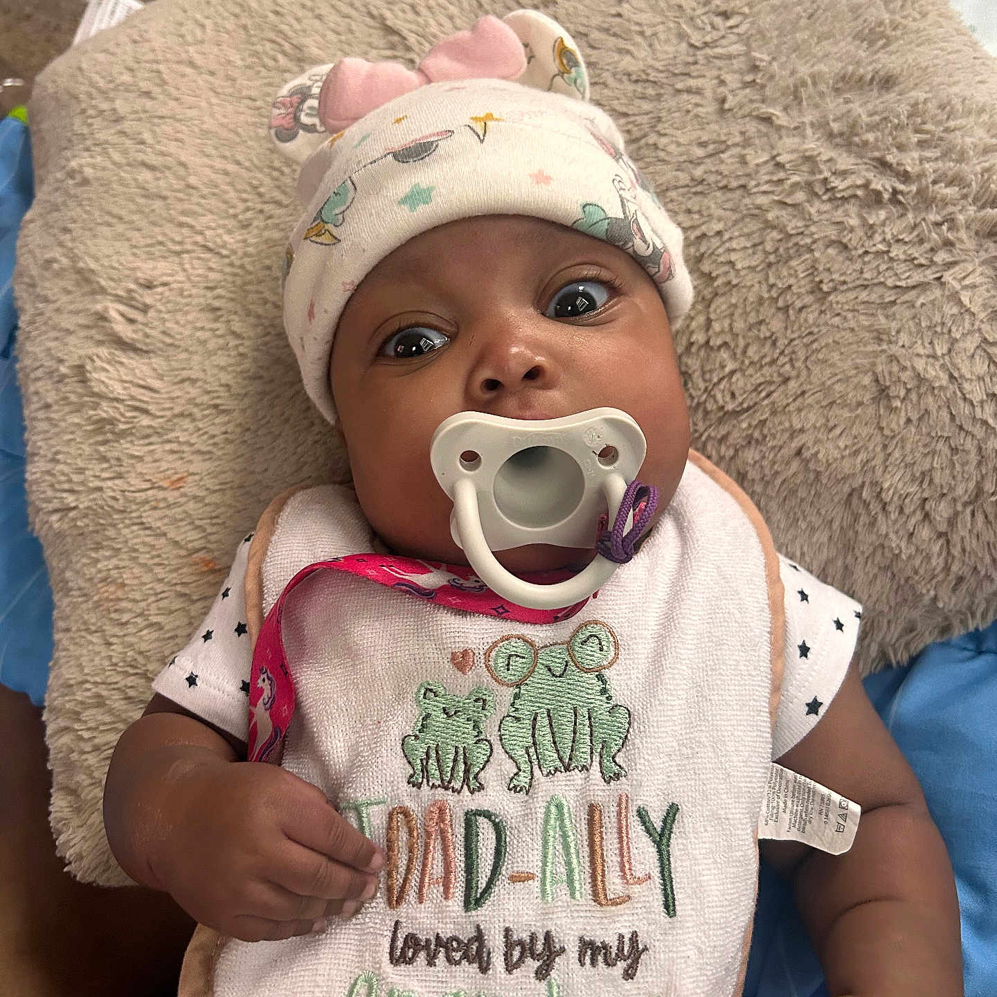 Kloni is registered to the contest to win money with this photo: baby, infant, pacifier, bib, hat, cute, lying_down, pillow, patterned_clothing, hand, indoor, closeup, portrait, child, adorable, soft_texture, sleepwear, expression, newborn, young_child