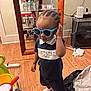 Jiaie is registered to the contest to win money with this photo: cabinet, casual, child, clothing, cord, elephant_figurine, floor, furniture, glassware, hair, indoor, person, power_strip, shirt, sock, storage, sunglasses, toddler, toy, wooden_floor