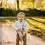 Sandro a rejoint le concours — aidez-le/la à gagner de superbes lots ! toddler, child, outdoor, pathway, autumn, leaves, tree, sunlight, toy, clothing, white_jacket, brown_pants, shoes, nature, smiling, person, standing, daylight, happy, casual