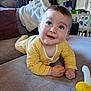 baby, child, infant, yellow_striped_clothing, couch, indoor, face, happy, smiling, hands, blue_eyes, curly_hair, blanket, pillow, home, living_room, toy, playful, portrait, cozy