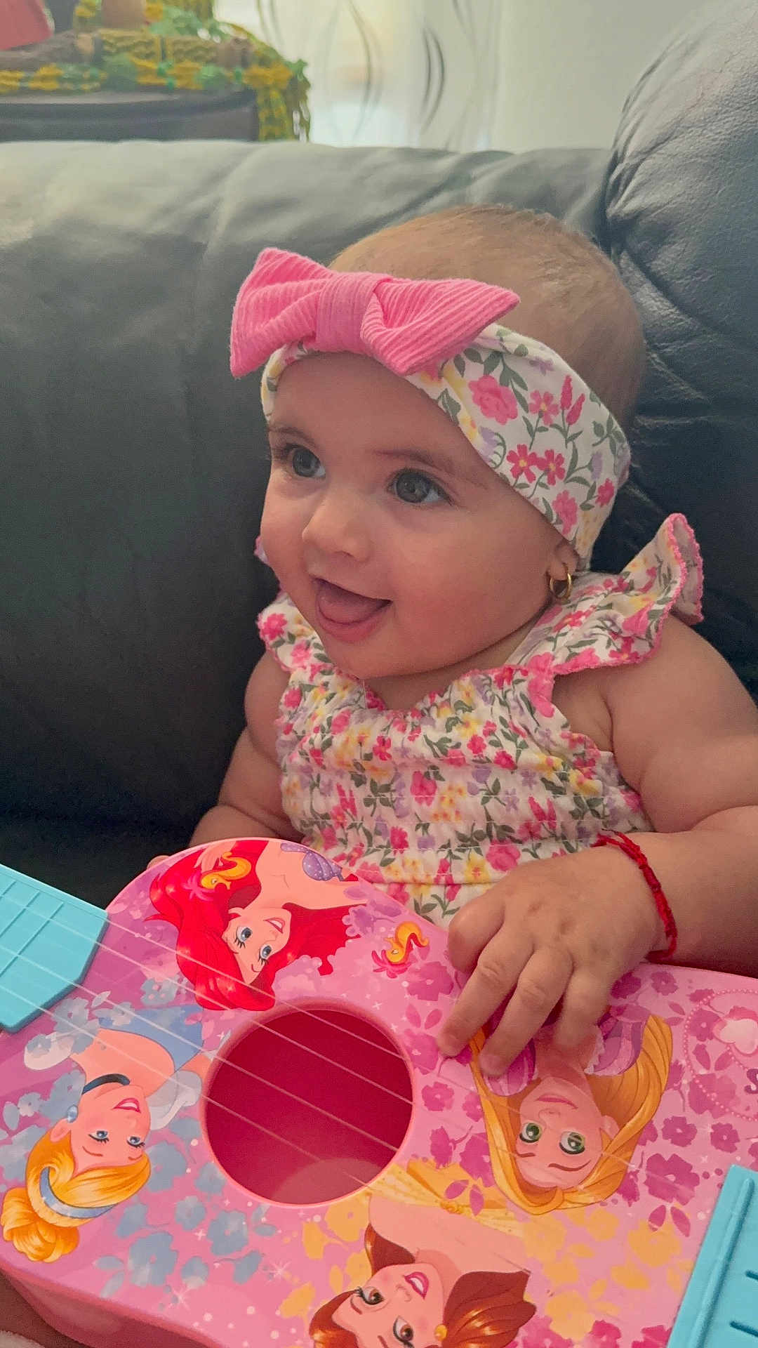 Ishtar is registered to the contest to win money with this photo: baby, child, girl, headband, pink_bow, floral_dress, toy_guitar, princess, couch, happy, smiling, indoor, playing, cute, earrings, red_bracelet, closeup, person, infant, music