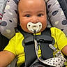 Zade is registered to the contest to win money with this photo: baby, car_seat, pacifier, child, yellow_shirt, black_shorts, seatbelt, headrest, patterned_cushion, infant, safety, cute, smiling, indoors, portrait, closeup, child_seat, happy, straps, young_child
