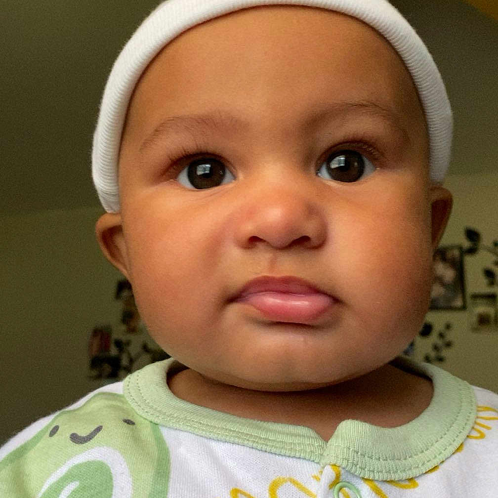 Zade joined the competition — help win amazing prizes! baby, infant, child, face, headwear, onesie, avocado_print, cute, indoors, ceiling_fan, portrait, expression, curious, pout, clothing, person, young_child, closeup, hat, room
