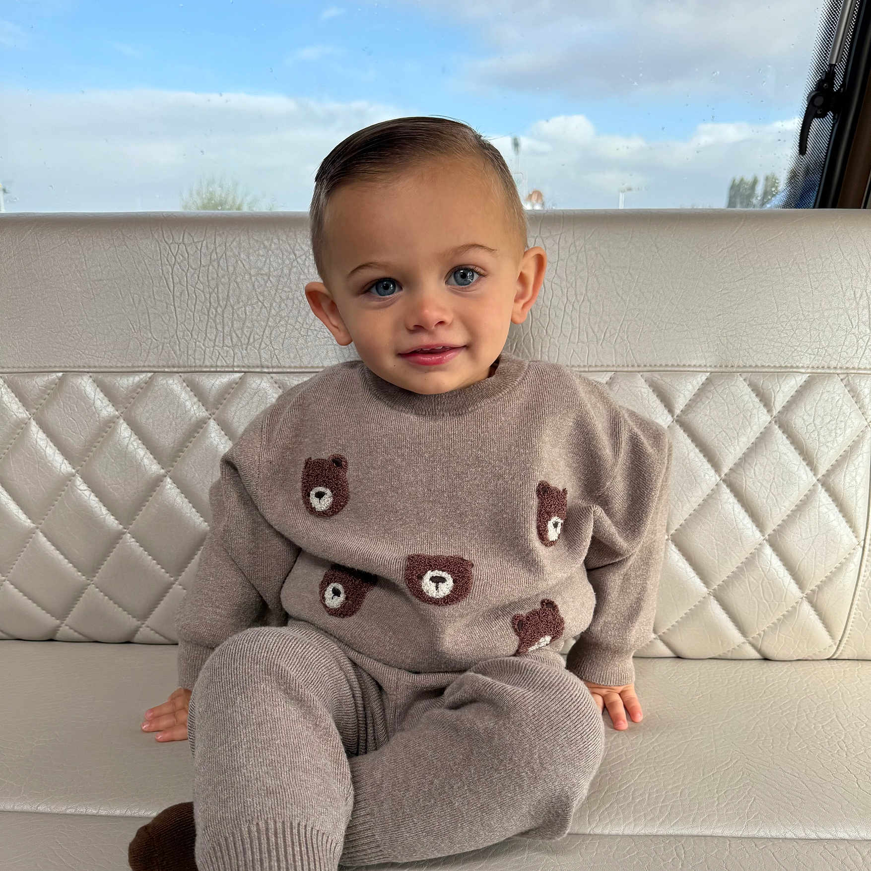 ésaïe a rejoint le concours — aidez-le/la à gagner de superbes lots ! bear_pattern, blue_eyes, boy, child, clouds, cozy, cute, hair, hand, indoor, leather, pants, portrait, quilted_bench, sitting, sky, smiling, sweater, toddler, window
