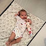 adorable, baby, baby_clothes, baby_girl, bedding, child, crib, cute, happy, indoors, infant, lying_down, onesie, patterned_bedding, person, playful, plush_toy, resting, smiling, soft_toy