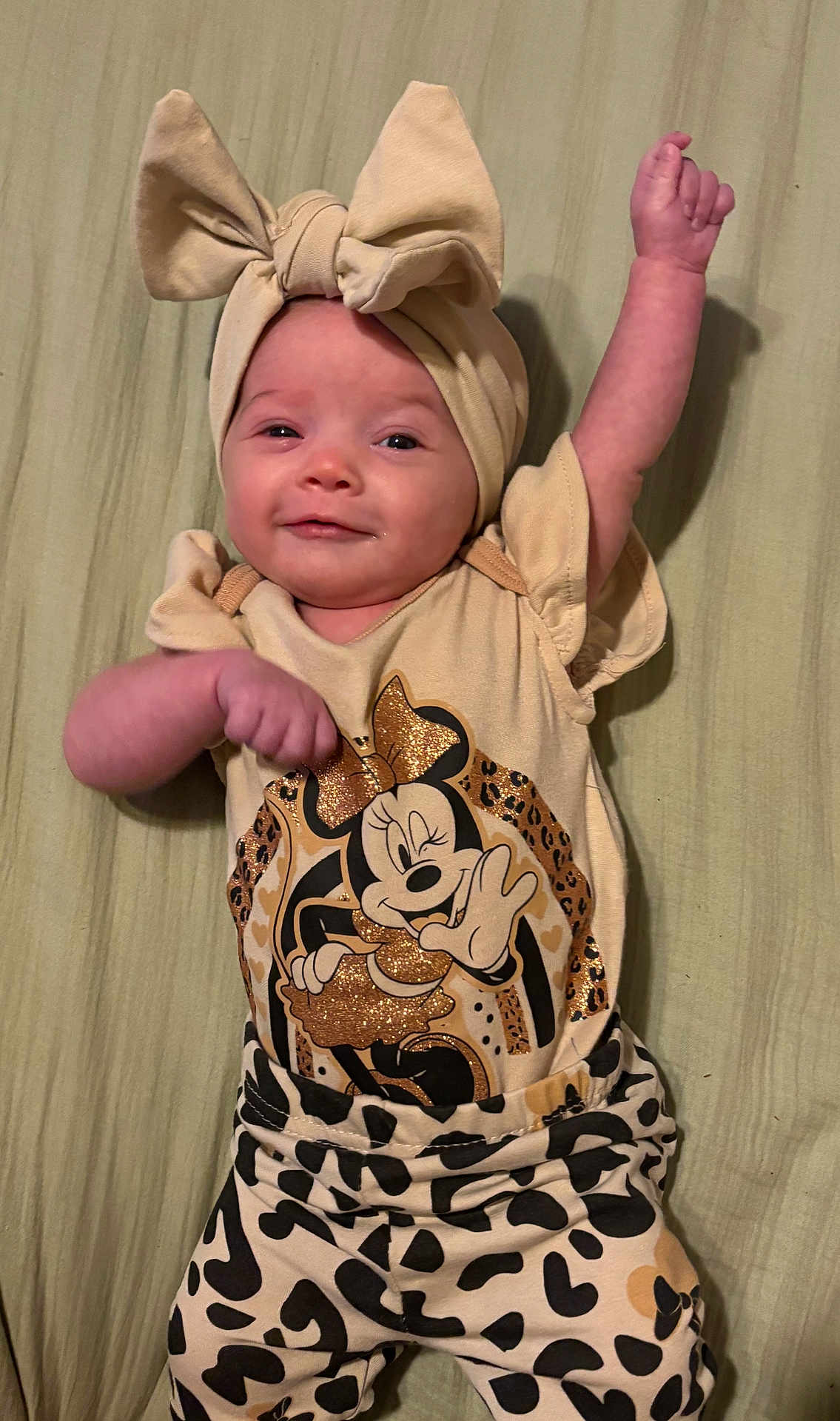 Liyana joined the competition — help win amazing prizes! baby, child, headband, bow, smile, minnie_mouse, cartoon, clothing, patterned_pants, animal_print, cute, infant, lying_down, raised_arm, happy, face, person, soft_surface, apparel, fashion