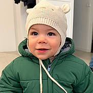 Qassim participe au concours pour gagner de l'argent avec cette photo : toddler, child, hat, knitted_hat, bear_ears, green_jacket, coat, indoor, portrait, smile, face, curious, young_child, cute, warm_clothing, baby, person, closeup, headwear, winter_wear