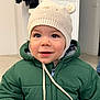 toddler, child, hat, knitted_hat, bear_ears, green_jacket, coat, indoor, portrait, smile, face, curious, young_child, cute, warm_clothing, baby, person, closeup, headwear, winter_wear