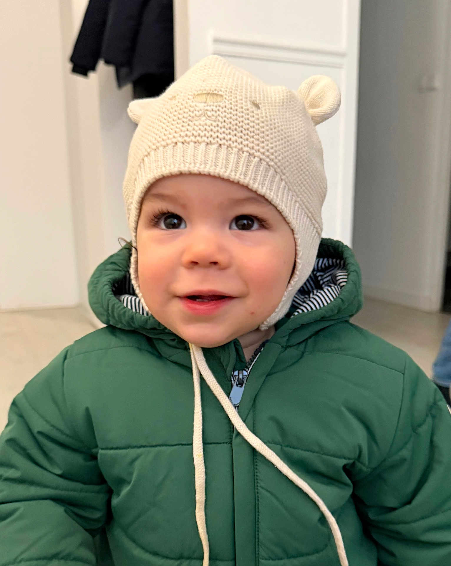 Qassim participe au concours pour gagner de l'argent avec cette photo : toddler, child, hat, knitted_hat, bear_ears, green_jacket, coat, indoor, portrait, smile, face, curious, young_child, cute, warm_clothing, baby, person, closeup, headwear, winter_wear
