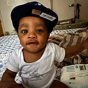 Dwane joined the competition — help win amazing prizes! baby, cap, hat, infant, child, bed, blanket, clothing, diapers, hand, indoor, person, face, expression, cute, curious, room, furniture, pattern, sitting