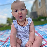 Audrey is registered to the contest to win money with this photo: baby, child, infant, outdoor, blanket, blue_sky, grass, house, necklace, sitting, cute, patterned_clothing, happy, portrait, smiling, fingers, feet, face, summer, sunlight