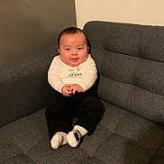 Nyingjey a rejoint le concours — aidez-le/la à gagner de superbes lots ! baby, black_pants, child, clothing, couch, cozy, cute, face, furniture, happy, home, indoor, person, portrait, sitting, smiling, socks, sofa, toddler, white_shirt