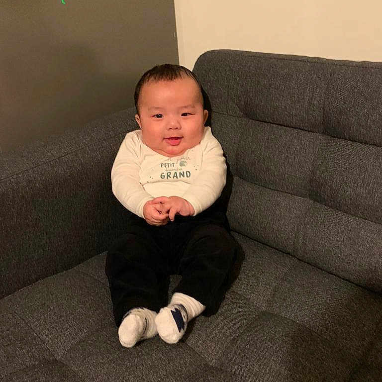 Nyingjey a rejoint le concours — aidez-le/la à gagner de superbes lots ! baby, black_pants, child, clothing, couch, cozy, cute, face, furniture, happy, home, indoor, person, portrait, sitting, smiling, socks, sofa, toddler, white_shirt