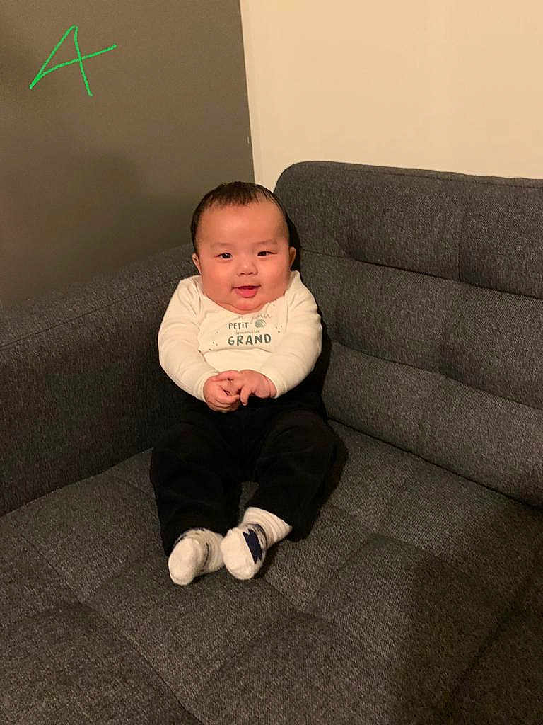 Nyingjey a rejoint le concours — aidez-le/la à gagner de superbes lots ! baby, black_pants, child, clothing, couch, cozy, cute, face, furniture, happy, home, indoor, person, portrait, sitting, smiling, socks, sofa, toddler, white_shirt