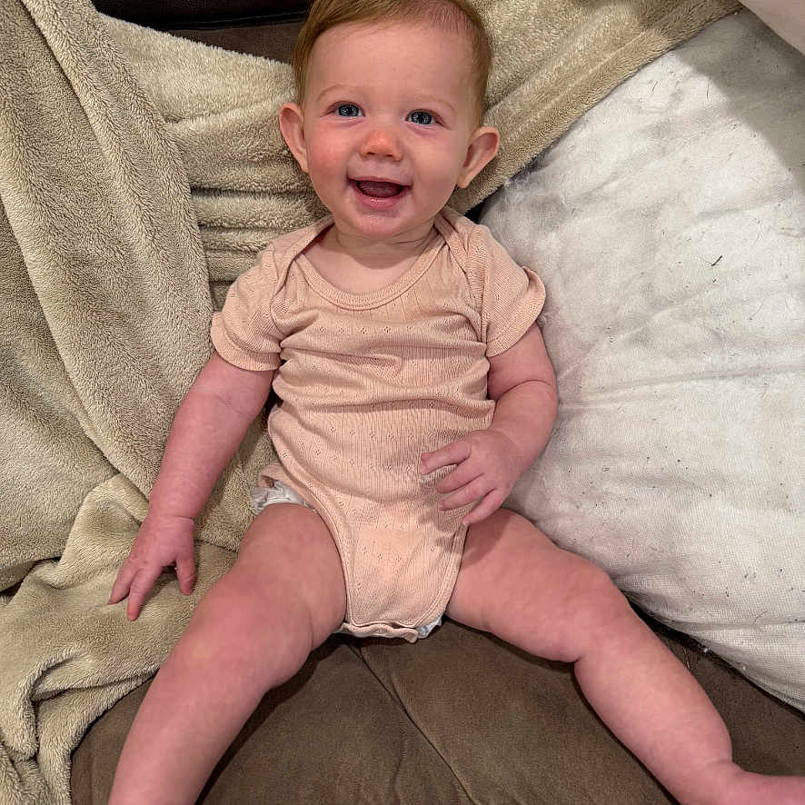 Drew joined the competition — help win amazing prizes! baby, infant, smiling, onesie, couch, blanket, indoor, child, happy, person, seated, cute, skin, head, face, legs, furniture, cozy, comfortable, young
