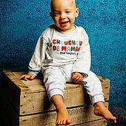 Nino a rejoint le concours — aidez-le/la à gagner de superbes lots ! toddler, child, smiling, barefoot, wooden_crate, sweater, clothing, blue_background, indoor, portrait, happy, cute, studio_lighting, floor_rug, baby, sitting, person, face, head, casual