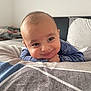 baby, child, face, smile, blue_clothing, bed, pillow, blanket, indoor, portrait, cute, dinosaur_print, head, resting, happy, person, young_child, infant, cozy, room
