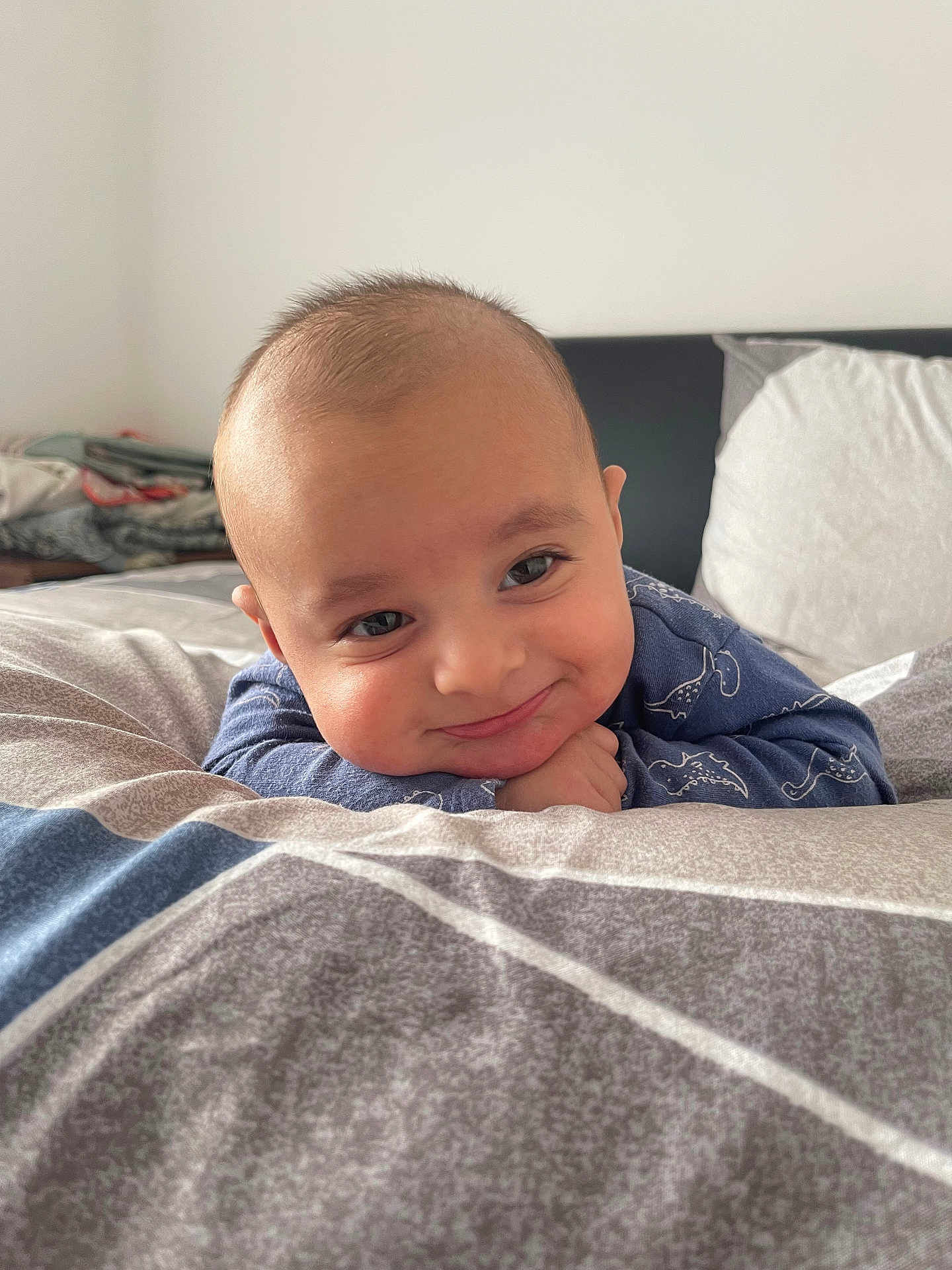 Ibrahim is registered to the contest to win money with this photo: baby, child, face, smile, blue_clothing, bed, pillow, blanket, indoor, portrait, cute, dinosaur_print, head, resting, happy, person, young_child, infant, cozy, room