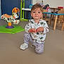 toddler, child, indoor, playroom, toy, dinosaur_clothing, kneeling, floor, table, chair, plastic_toy, colorful, young_child, person, casual_clothing, cute, play, baby, furniture, smiling