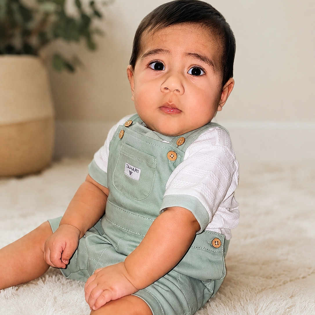 Kenai joined the competition — help win amazing prizes! baby, child, infant, sitting, overalls, white_shirt, carpet, indoor, plant, pot, cute, portrait, expression, skin, hair, furniture, floor, person, young, casual_clothing