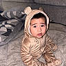 Kenai joined the competition — help win amazing prizes! baby, child, onesie, bear_costume, cute, indoor, pillow, quilt, soft_texture, seated, curious, wide_eyes, infant, face, cozy, plush, warm_colors, portrait, person, clothing