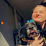person, dog, hugging, smile, sunlight, porch, tattoo, earrings, hoodie, black_dog, tongue_out, happy, closeup, outdoor, door, window, hand, heart_emoji, casual, home