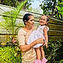elderly_woman, toddler, child, woman, smile, white_dress, pink_sandals, garden, plants, greenery, potted_plants, outdoor, nature, fence, portrait, holding, happy, family, person, casual_clothing