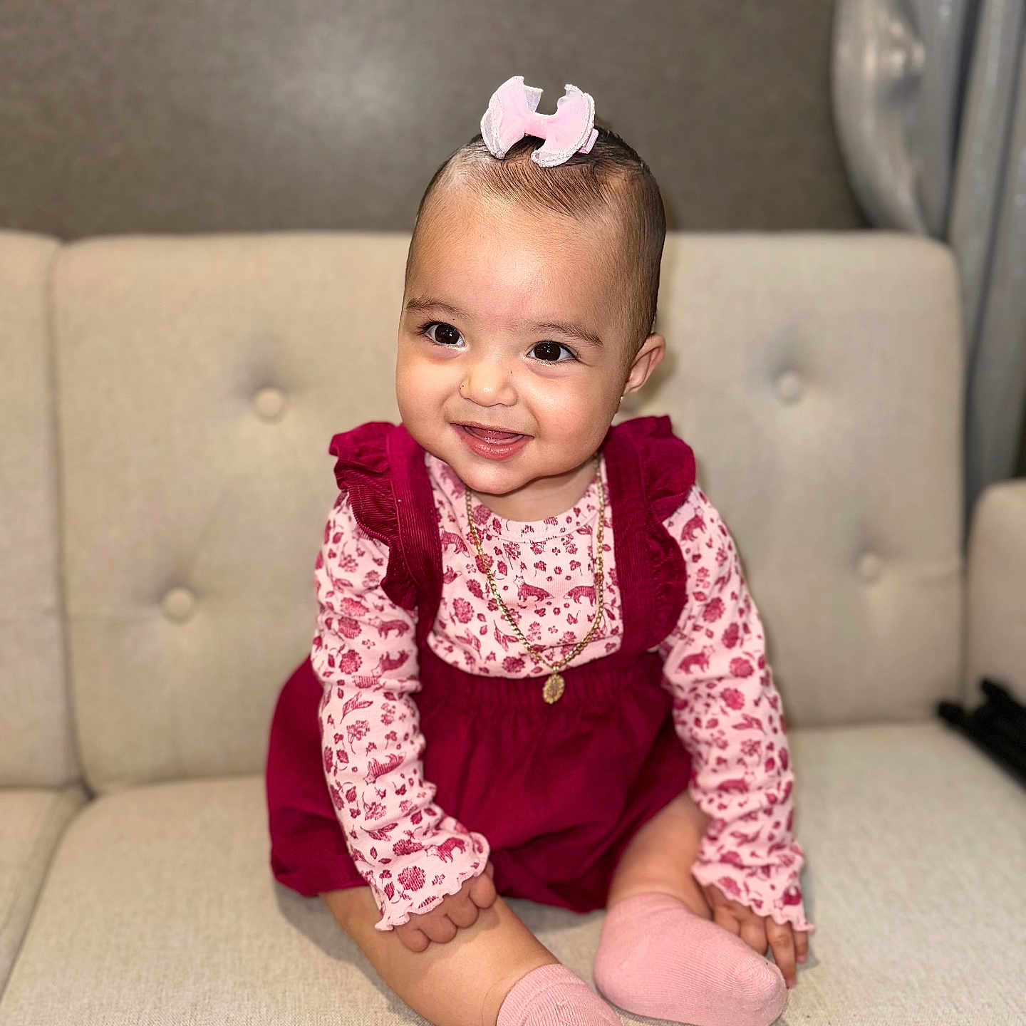 Isabella joined the competition — help win amazing prizes! baby, child, couch, cute, floral_outfit, furniture, gold_chain, happy, home, indoor, infant, jewelry, long_sleeve, person, pink_bow, pink_socks, portrait, sitting, smile, toddler