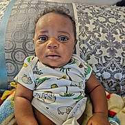 Franklin joined the competition — help win amazing prizes! baby, infant, child, onesie, blanket, couch, patterned, animal_print, curly_hair, skin, hand, face, eyes, sitting, indoors, portrait, clothing, comfort, expression, young