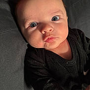 Colton is registered to the contest to win money with this photo: baby, infant, face, eyes, black_clothing, pout, close_up, portrait, child, young, cute, skin, expression, lying_down, indoor, fabric, red_background, soft_light, person, newborn