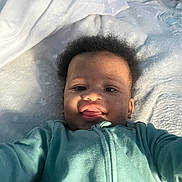 Chavezz joined the competition — help win amazing prizes! baby, child, infant, onesie, teal_clothing, blanket, bed, face, tongue, smile, happy, curly_hair, skin, portrait, lying_down, young_child, cute, indoors, soft_light, cozy