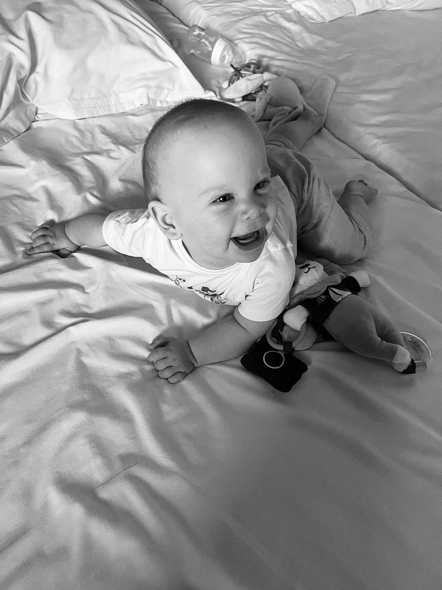 Sacha a rejoint le concours — aidez-le/la à gagner de superbes lots ! baby, smiling, bed, blanket, stuffed_toy, clothing, happy, infant, face, person, indoors, cute, child, lying_down, soft, monochrome, toddler, playful, comfort, toy