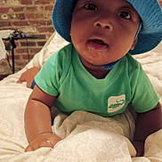 Cameron is registered to the contest to win money with this photo: baby, bed, blanket, blue_hat, brick_wall, child, curious, cute, expression, face, green_shirt, headwear, indoor, infant, lying_down, person, portrait, skin, toddler, young