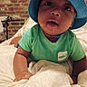 baby, bed, blanket, blue_hat, brick_wall, child, curious, cute, expression, face, green_shirt, headwear, indoor, infant, lying_down, person, portrait, skin, toddler, young