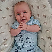 Jan is registered to the contest to win money with this photo: baby, smiling, blue_outfit, blanket, rainbow_pattern, infant, clothing, cute, happy, hand_position, lying_down, portrait, child, person, soft_texture, indoors, face, head, skin, young