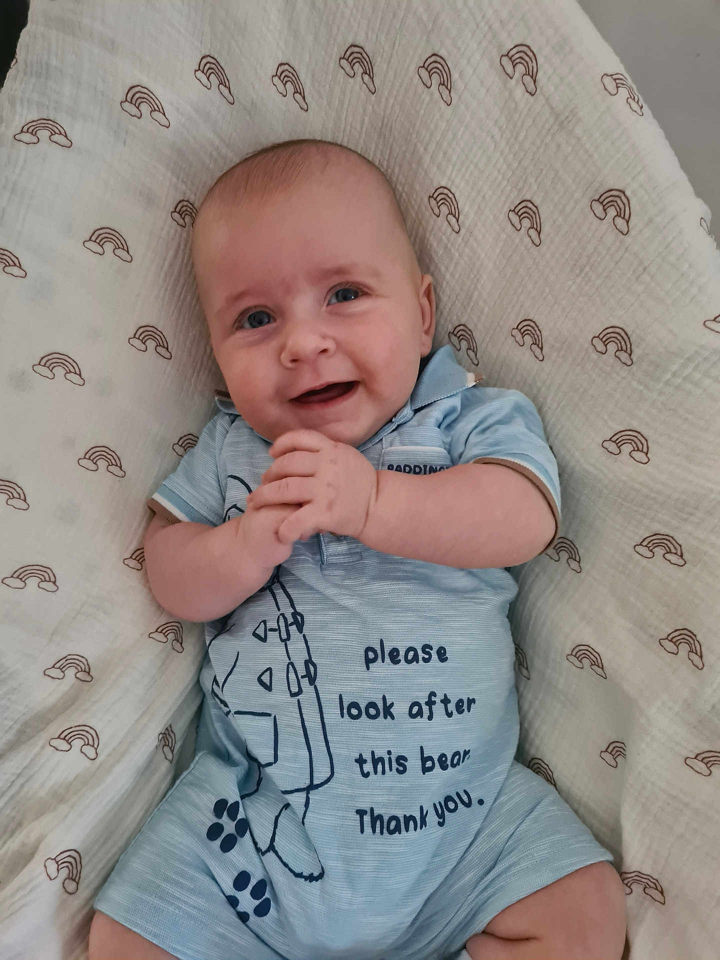 Jan is registered to the contest to win money with this photo: baby, smiling, blue_outfit, blanket, rainbow_pattern, infant, clothing, cute, happy, hand_position, lying_down, portrait, child, person, soft_texture, indoors, face, head, skin, young