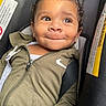 toddler, child, curly_hair, car_seat, hoodie, smile, face, baby, seat_belt, clothing, zipper, indoor, cute, portrait, young_child, person, expression, sitting, close_up, happy