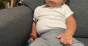 Adonis is registered to the contest to win money with this photo: baby, child, couch, curly_hair, cute, expression, furniture, gray_couch, gray_pants, home, indoor, person, plant, portrait, relaxed, seated, toddler, toy, white_shirt, young_child