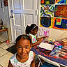 Queani is registered to the contest to win money with this photo: activity, art, chair, child, colorful, curly_hair, door, drawing, floor_tile, furniture, girl, happy, headband, indoor, markers, painting, person, smile, table, wall_art